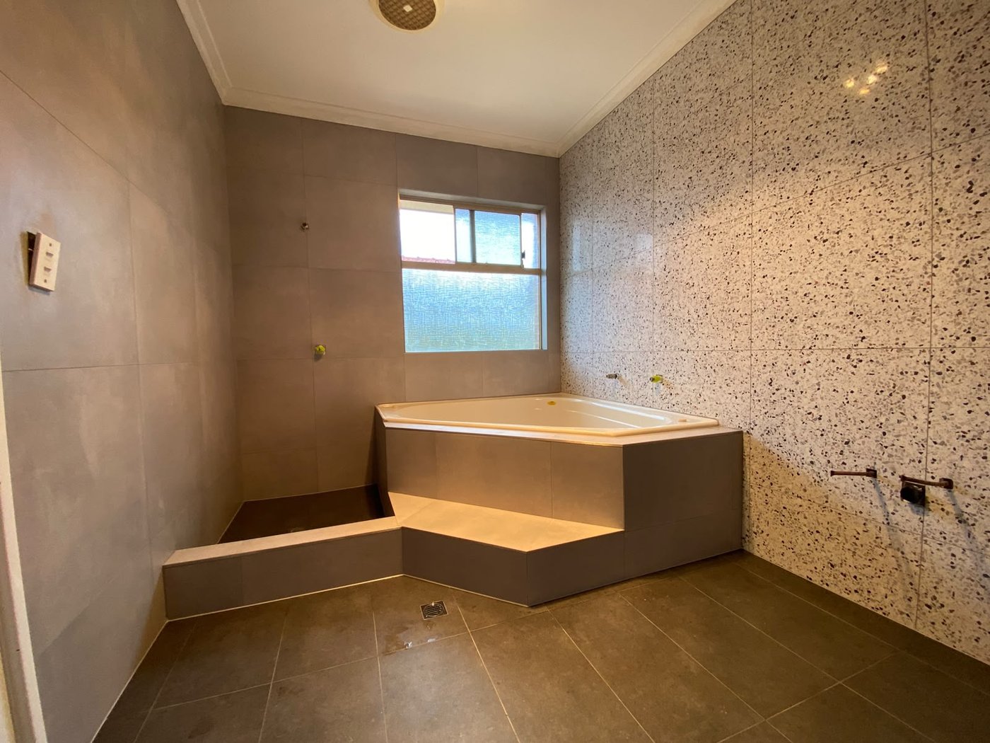 Corner spa bath with terrazzo feature wall and large-format tiling in a Perth bathroom
